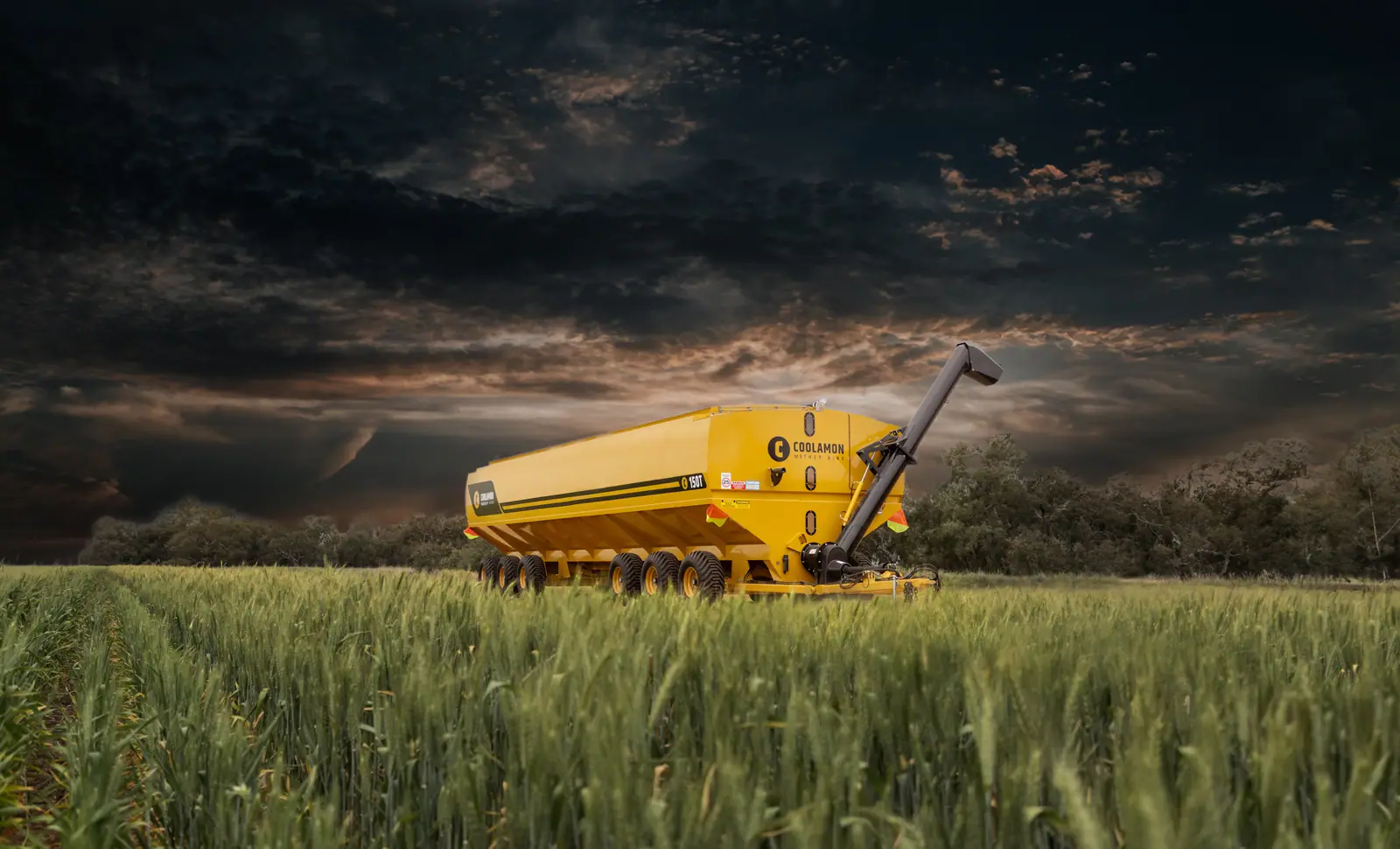 Yellow Coolamon Mother Bins grain cart in a crop field beneath a dramatic stormy sky