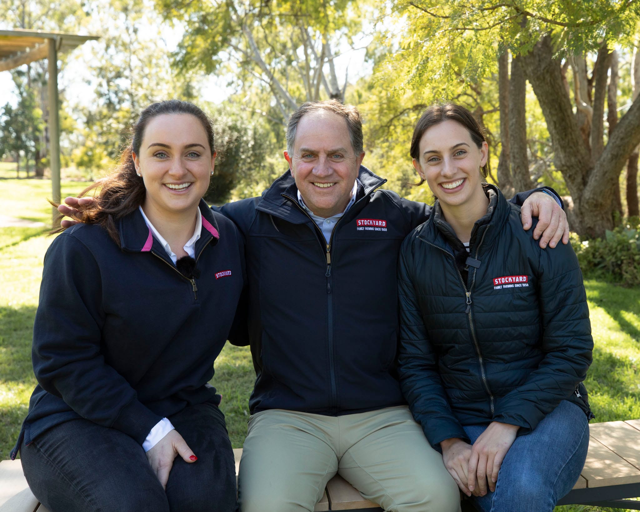 Three Stockyard Beef team members sitting together outdoors in branded jackets