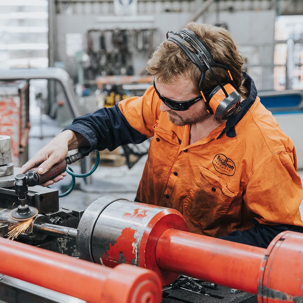 Bendcraft worker wearing safety glasses and hearing protection while polishing a metal pipe in a workshop