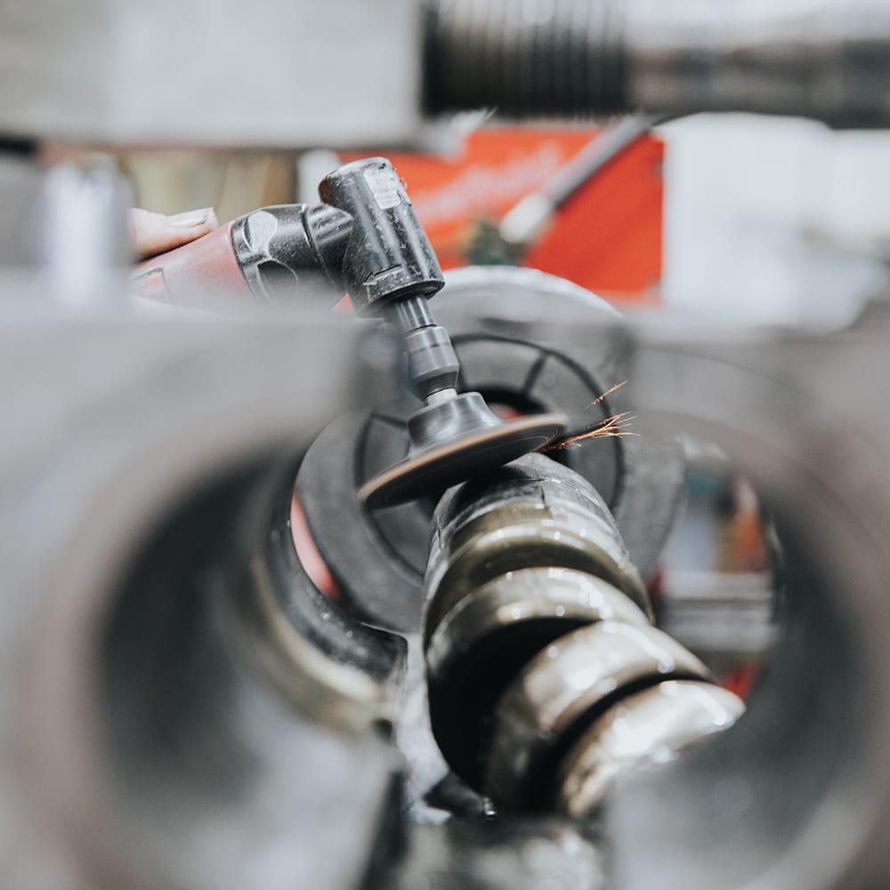 Close-up of a rotary tool polishing a metal pipe with small sparks