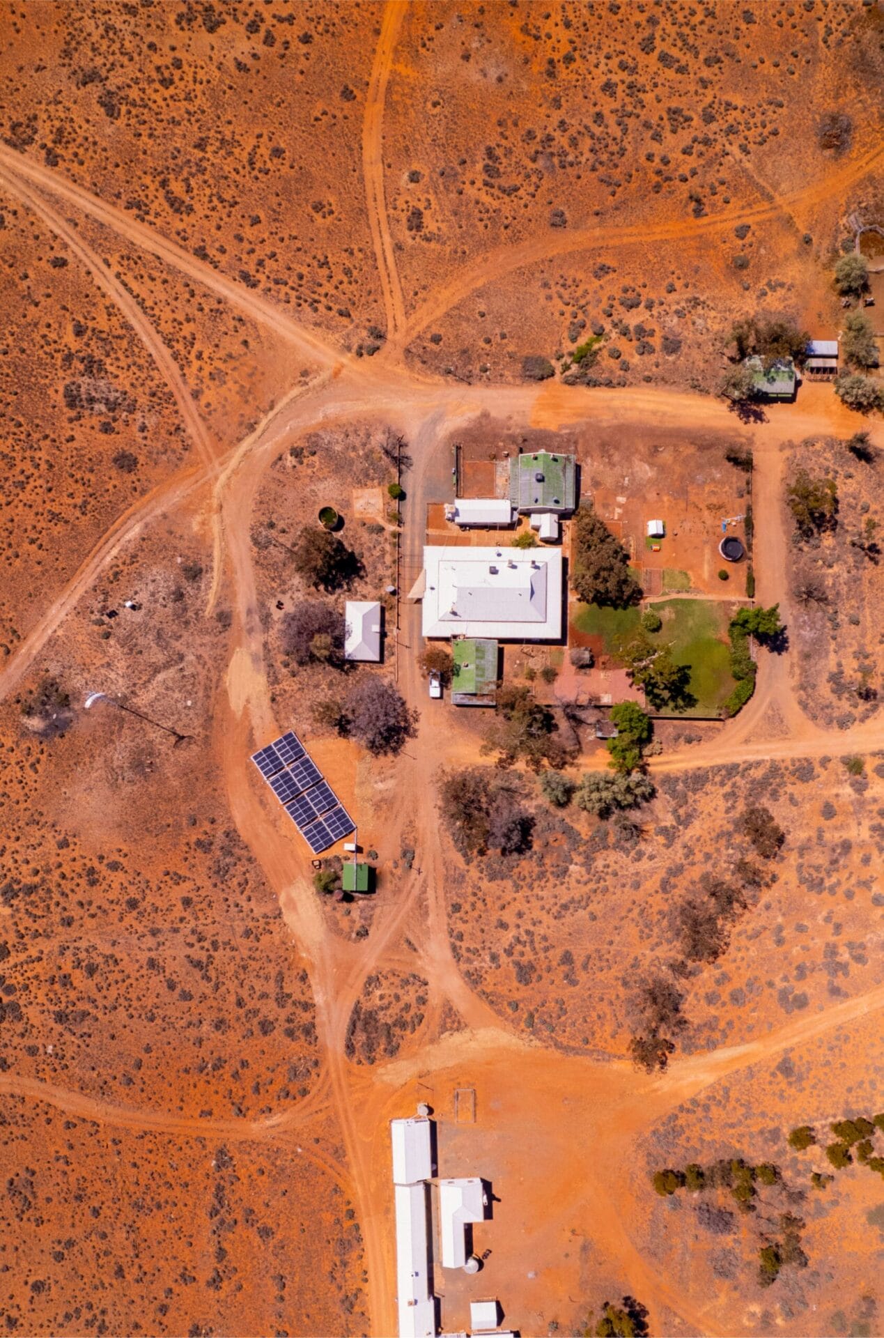Aerial view of a remote red dirt homestead with access tracks, outbuildings, and a ground-mounted solar array