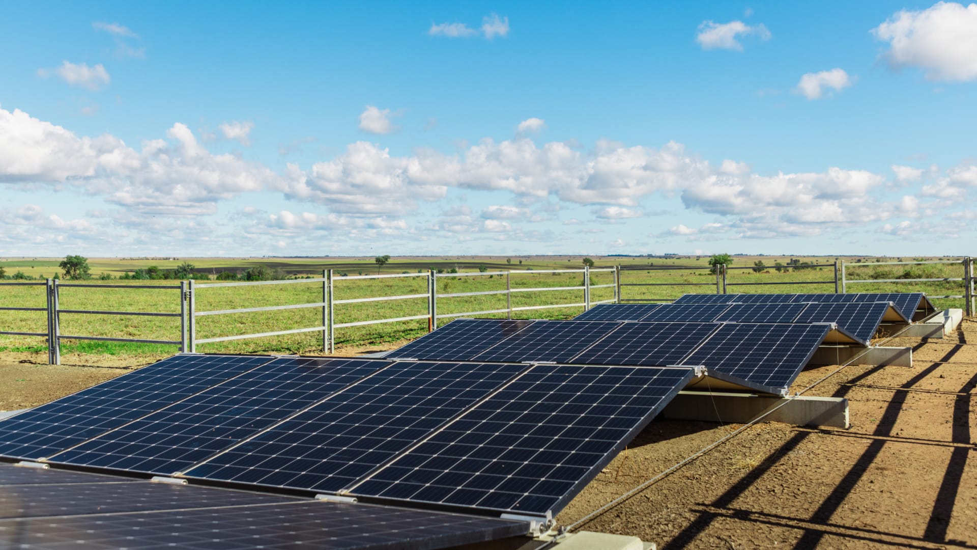 Ground-mounted solar panels installed in a fenced rural field under a blue sky