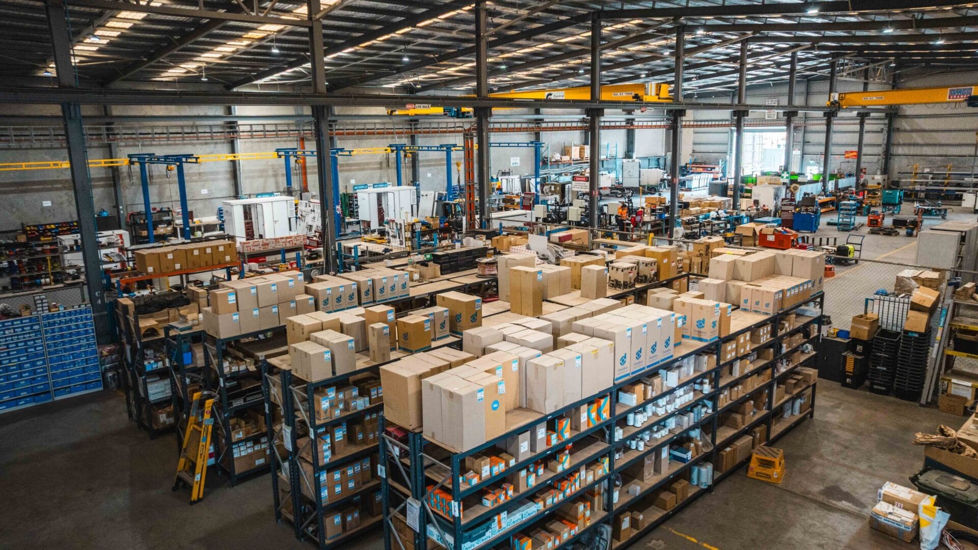 Large warehouse interior with stocked shelves, boxed inventory, and industrial equipment