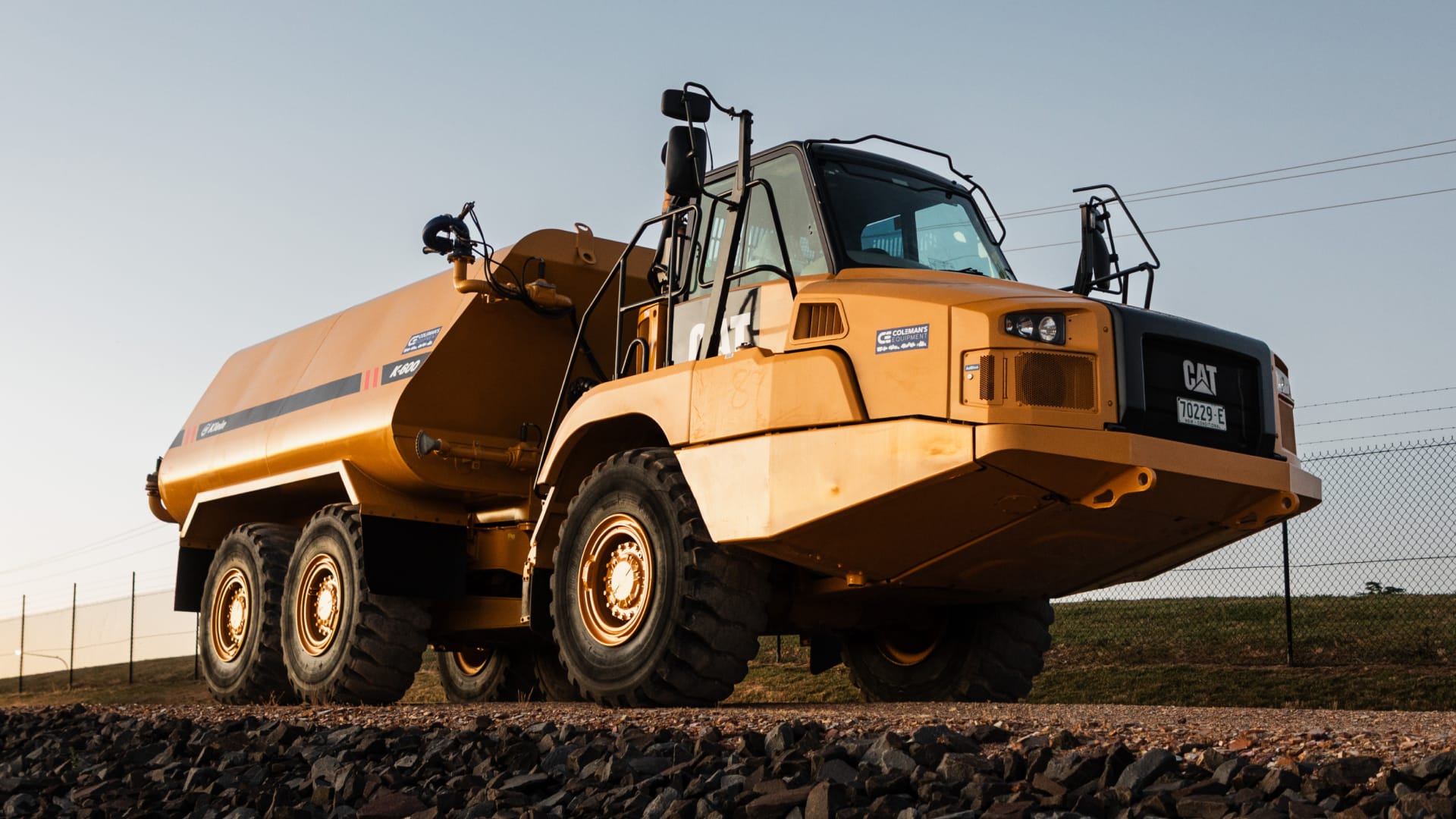 Low-angle yellow CAT water cart with heavy tyres on a gravel yard