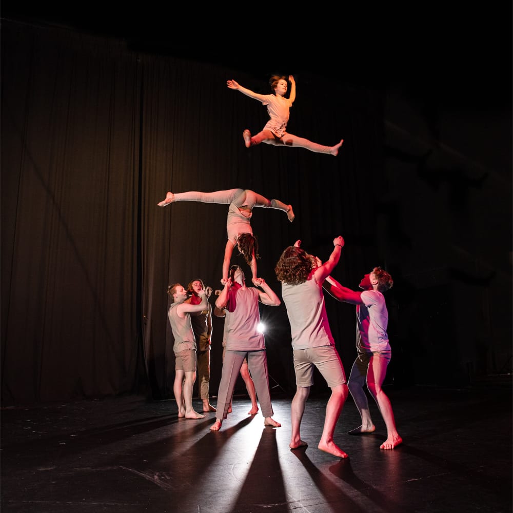 Young circus performers making an acrobatic lift on a dark stage under theatrical lighting