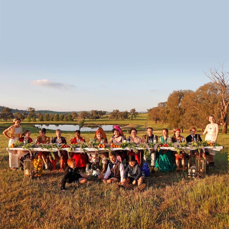 Hothouse Theatre cast group portrait at a decorated outdoor banquet table in a rural landscape