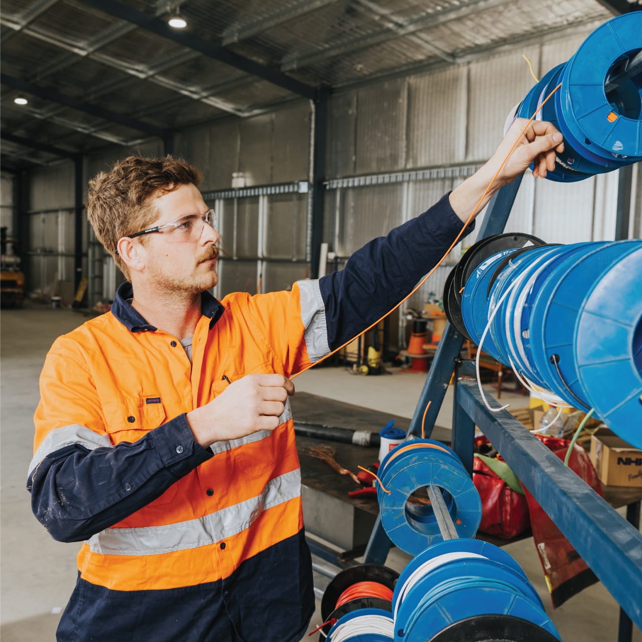 MBI Engineering technician wiring orange cable through blue cable reels inside a workshop