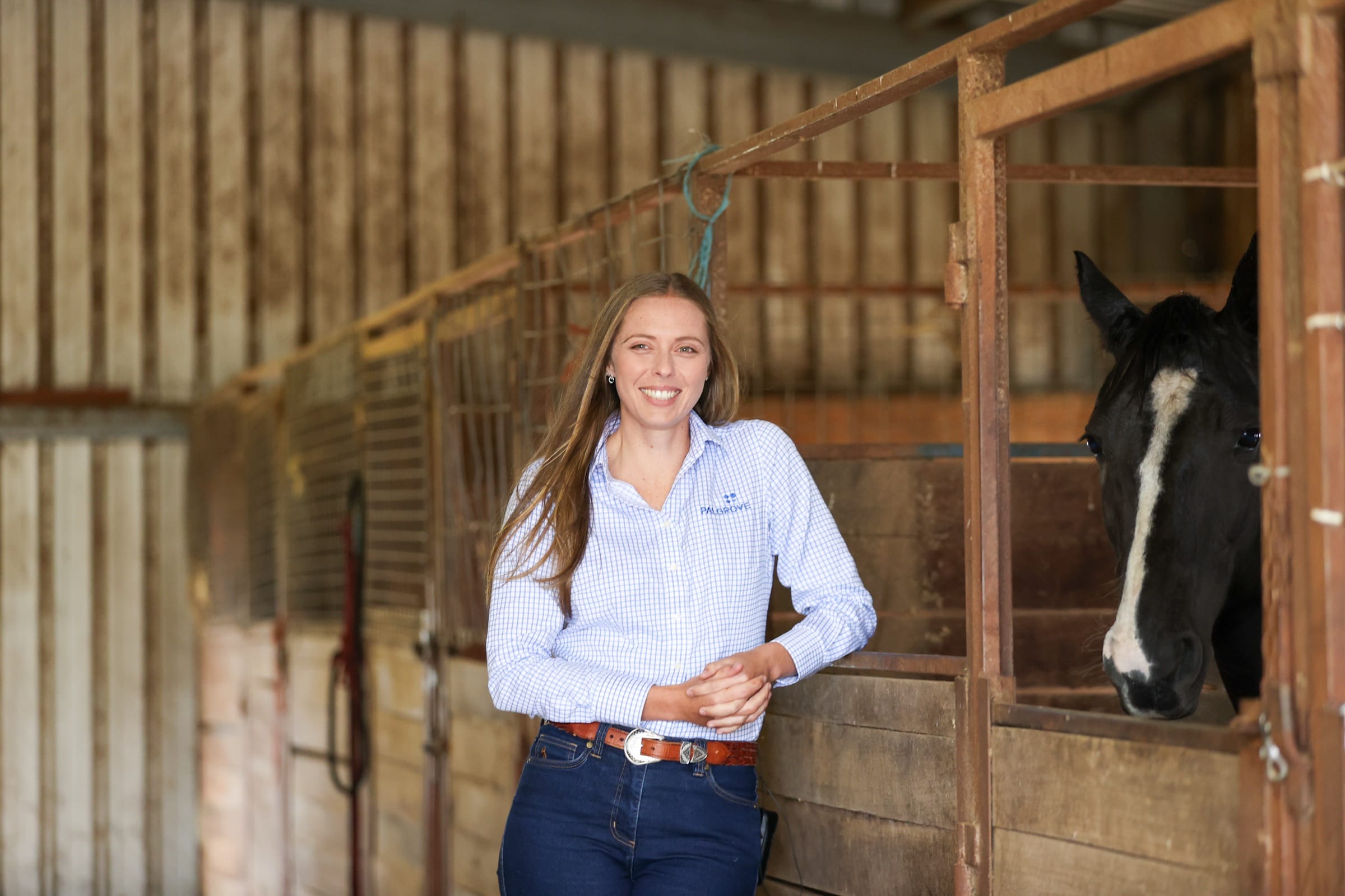 Palgrove stud team member smiling beside a bay horse at the entrance to a stable