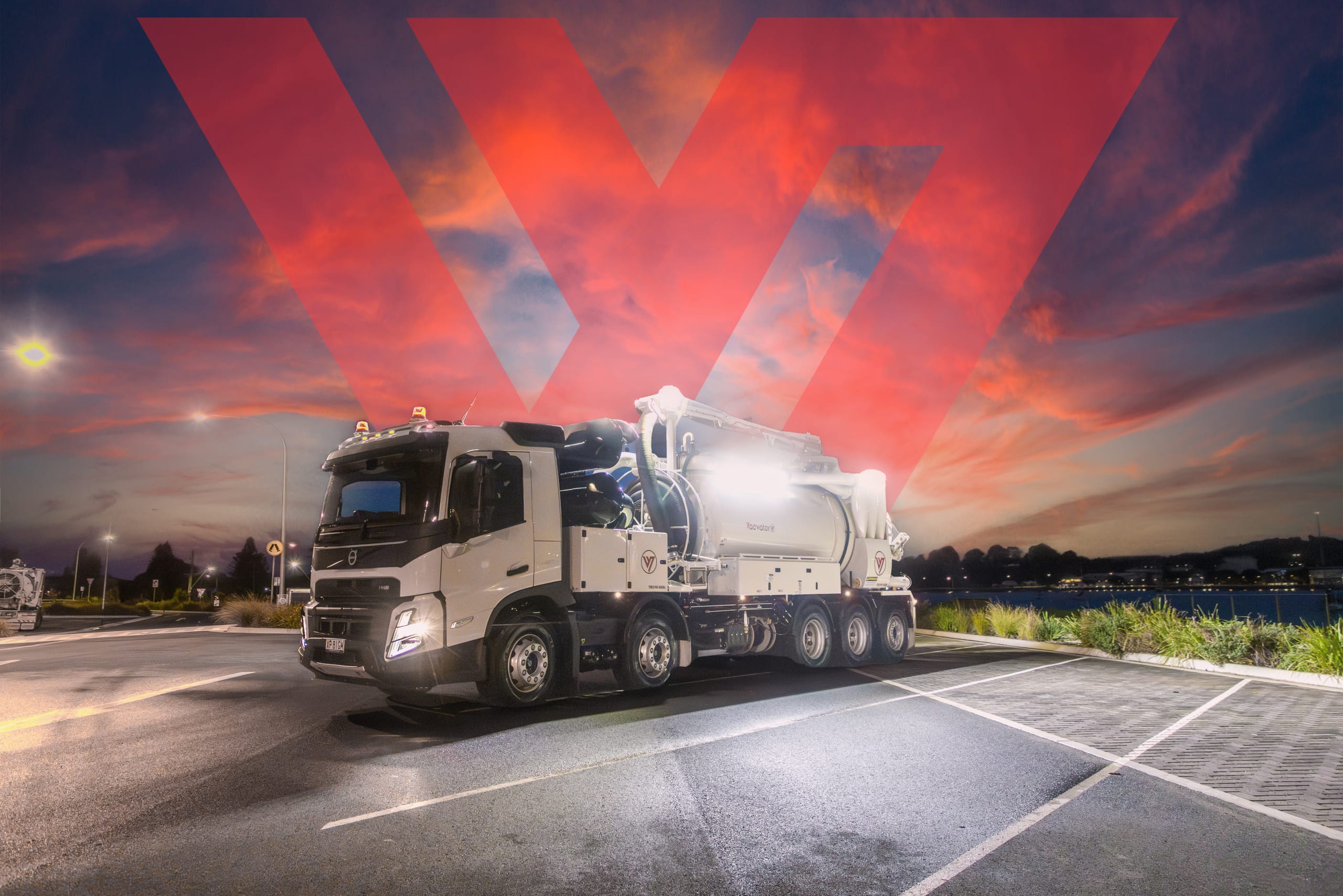 Vacvator vacuum truck at dusk with red logo lighting projected across the sky