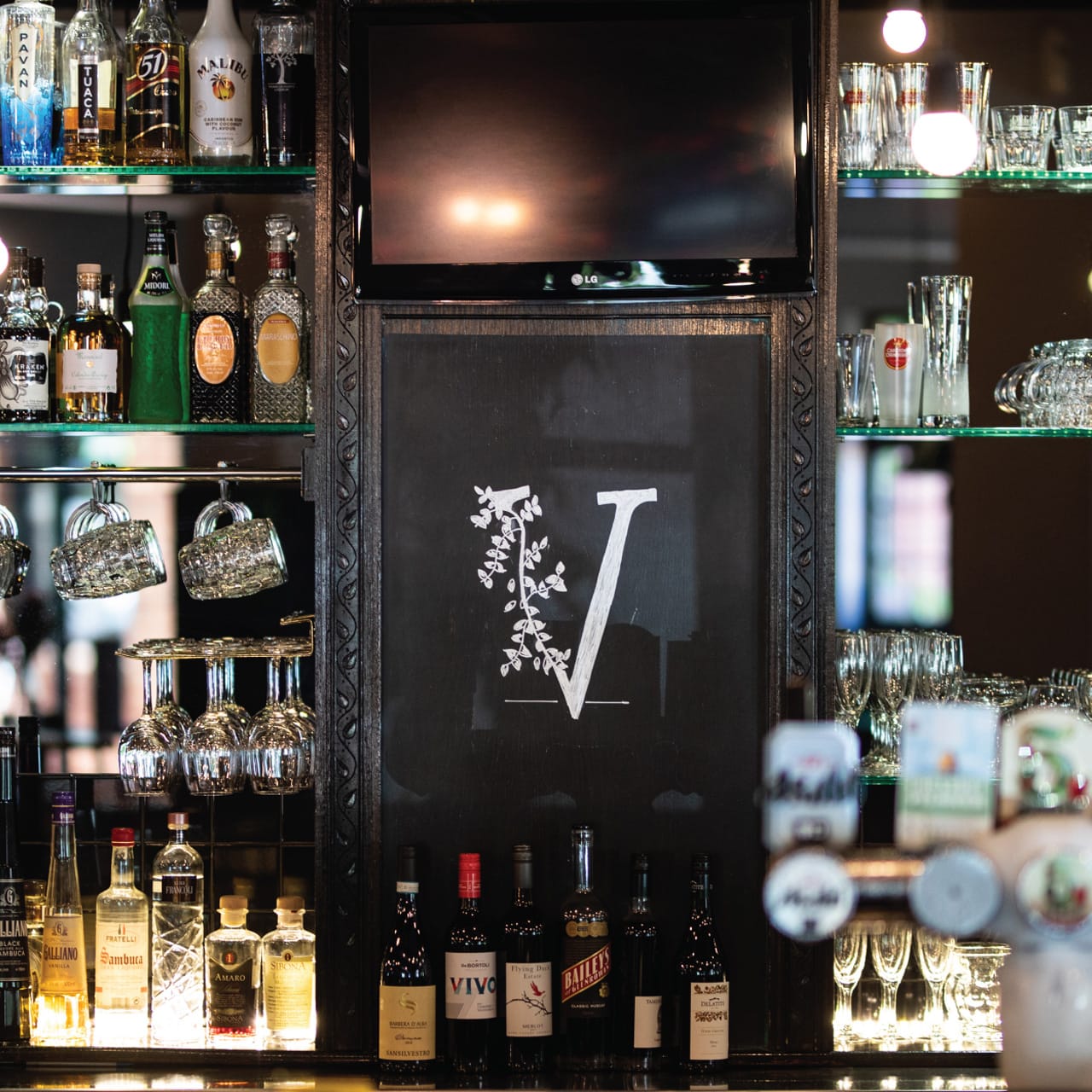 Victor's logo display surrounded by liquor bottles and glassware behind the bar