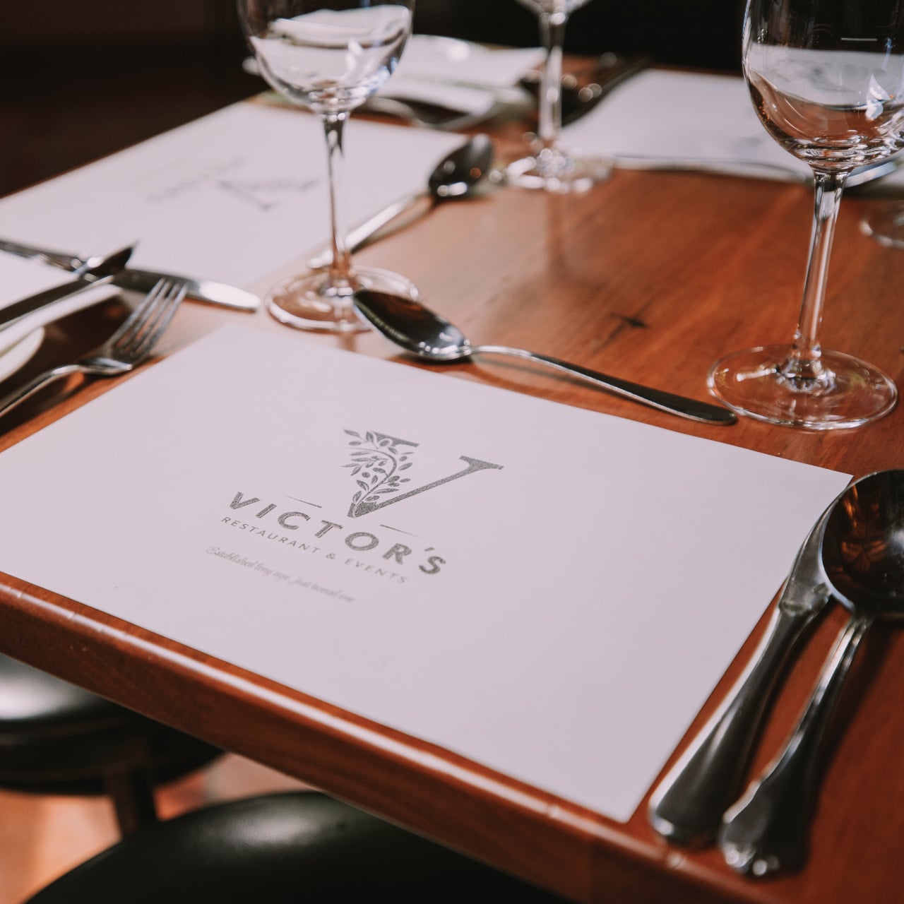 Victor's restaurant menu on a wooden dining table set with cutlery and wine glasses