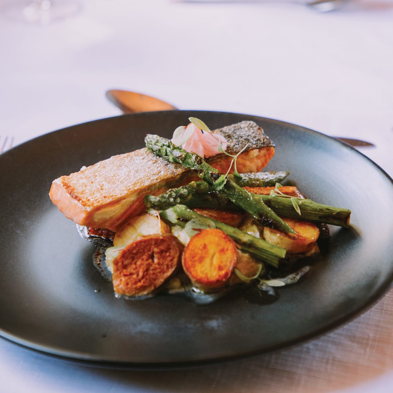 Seared salmon served with asparagus and roasted potatoes on a dark plate