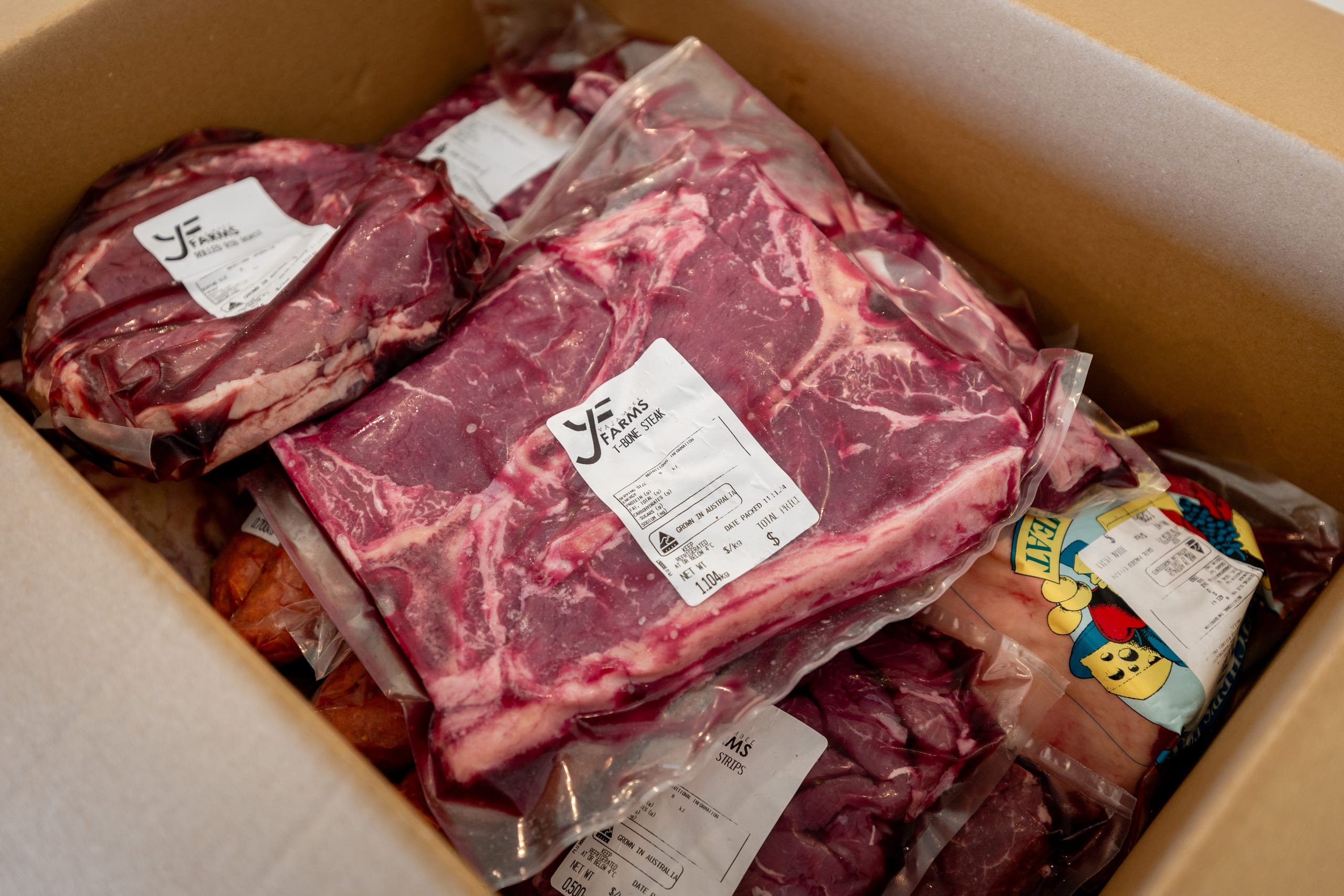 Box filled with vacuum-packed Yajambee Farms beef cuts, including a T-bone steak